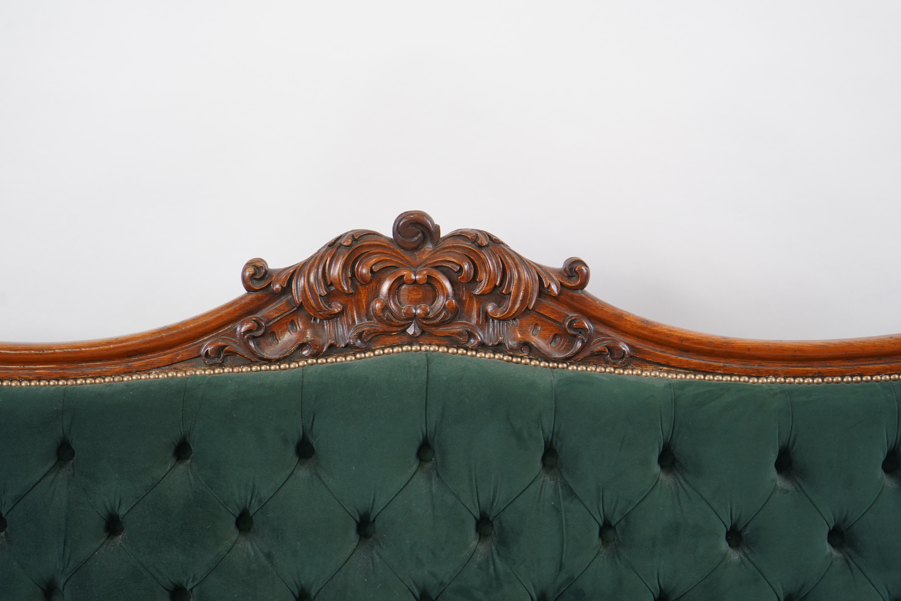 A pair of Victorian carved oak settees, recently re-upholstered in deep buttoned green velvet, the scroll carved crest rails over serpentine seats on cabriole front legs, 160cm wide, 96cm high, Provenance - previously gi